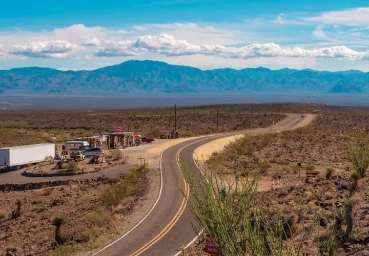 Droga Route 66 w pustynnym krajobrazie z budynkami i górami w tle.