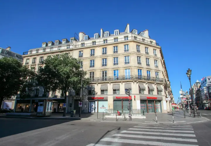 Elegancka kamienica przy rue de Rivoli w Paryżu, z markizami nad oknami i sklepem Foot Locker na parterze.