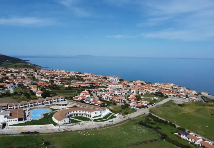 Widok z lotu ptaka na kurort GH Santina Resort z basenem i budynkami, nad morzem na Sardynii.