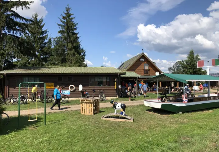 Na placu przed drewnianymi budynkami, wśród drzew, stoi łódź i krowa na moście. Je je jeleń witnica, jakby czekał na wycieczkę.