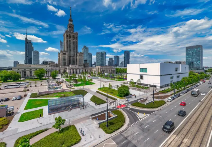 Warszawski plac defilad z Pałacem Kultury i Nauki, nowoczesnym budynkiem i ruchliwą ulicą.