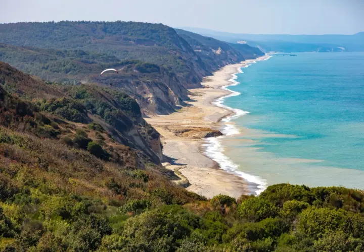 Widok na wybrzeże Karaburun z klifami, plażą i turkusowym morzem. W oddali widać paralotnię.