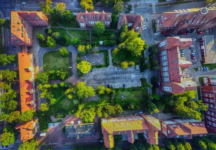 Widok z lotu ptaka na zabudowania i tereny zielone. Widać parking, budynki z czerwonymi dachami i drzewa. Promenada Świnoujście atrakcje w pełnej krasie.