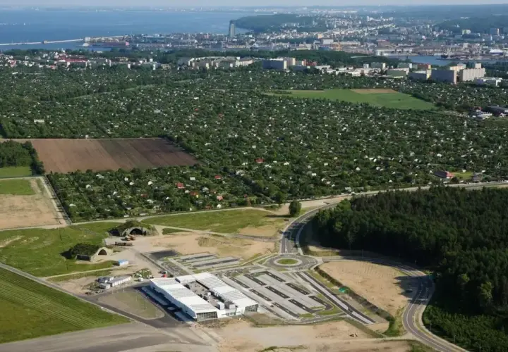 Widok na lotnisko Kosakowo z nowymi budynkami i drogami, w tle rozległe ogródki działkowe i panorama Gdyni.