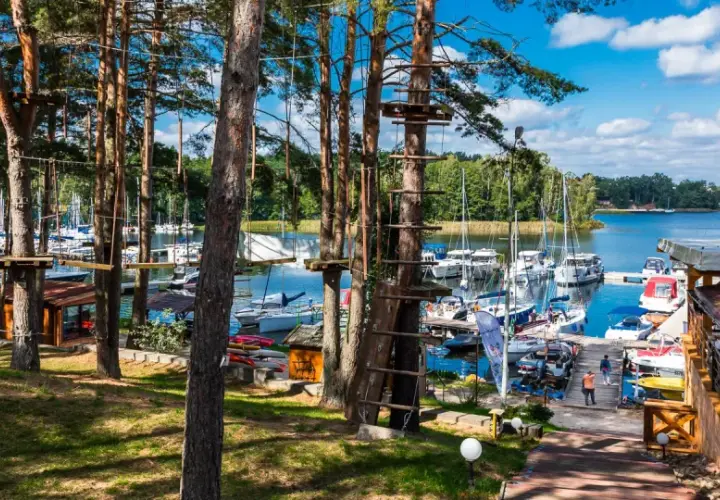 Linowy park rozrywki w lesie nad jeziorem z przystanią pełną jachtów.