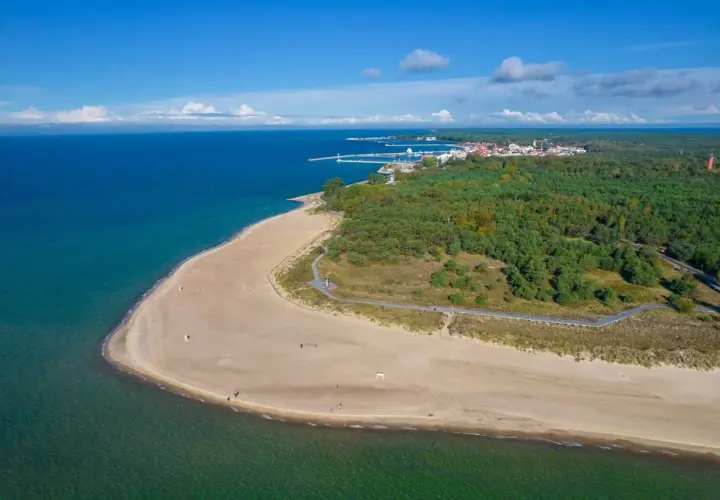 Piękny widok na piaszczystą plażę i turkusowe morze w Helu. W oddali widać miasteczko i las.