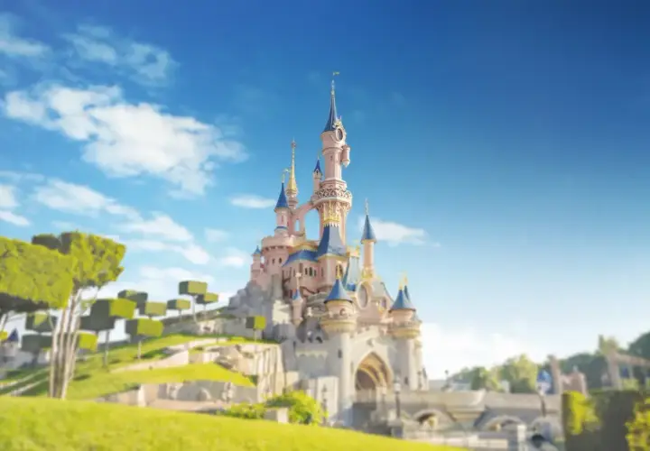 Zamek w Disneylandzie Paryż na tle błękitnego nieba z chmurami i zielonymi drzewami.
