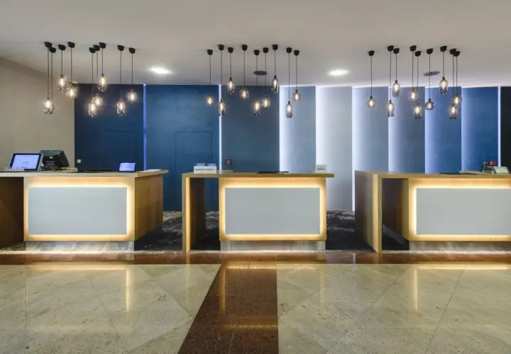 Recepcja hotelowa z trzema ladami, nowoczesnymi lampami i podświetlanymi panelami.