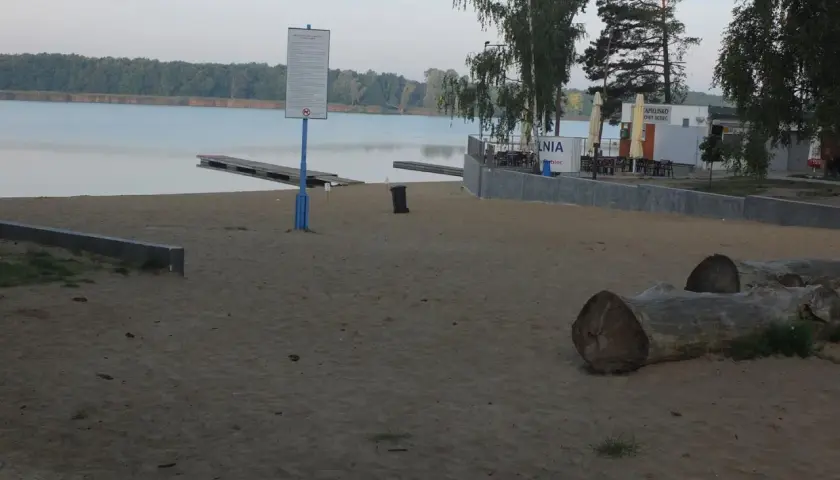 Plaża nad jeziorem Wonieść z pomostami, budynkiem kąpieliska i leżakami.