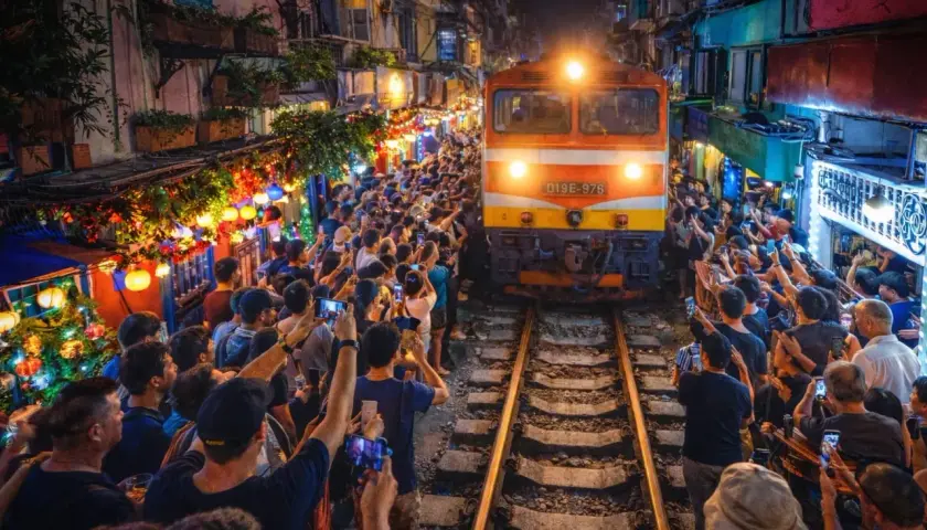 Pociąg przejeżdża wąską uliczką w Hanoi, otoczony tłumem ludzi z telefonami.