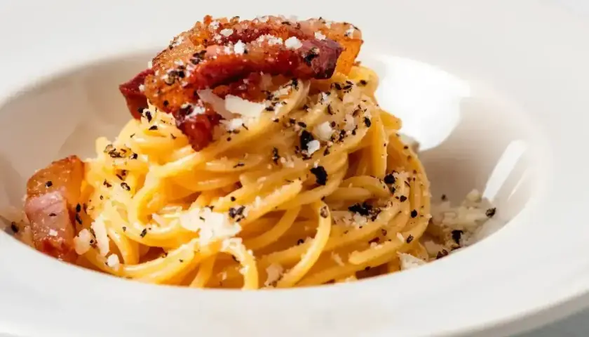 Pyszne spaghetti carbonara z chrupiącym guanciale, posypane parmezanem i czarnym pieprzem.