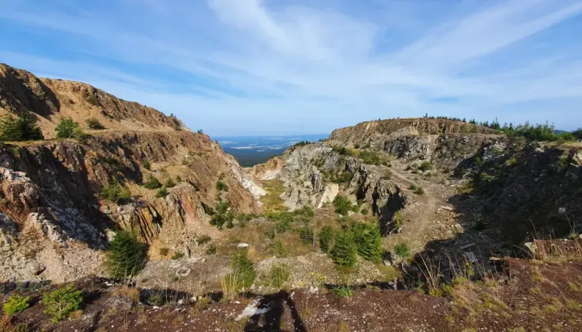 Krajobraz po wydobyciu kwarcu w kopalni Stanisław. Skarpy skalne, zarośla i niebo.