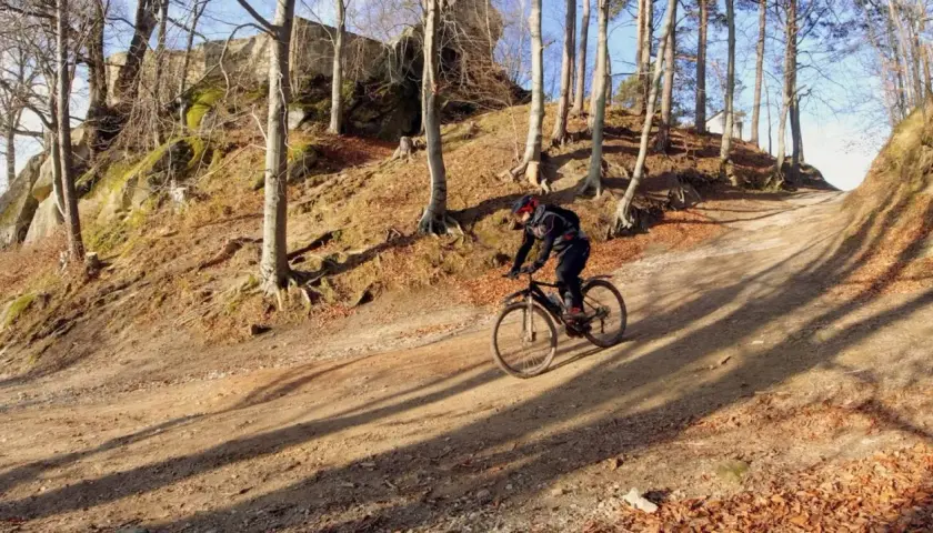 Rowerzysta na piaszczystej ścieżce wśród drzew. W tle skaliste zbocze porośnięte mchem. To jedne z wielu atrakcji Pogórza Dynowskiego.