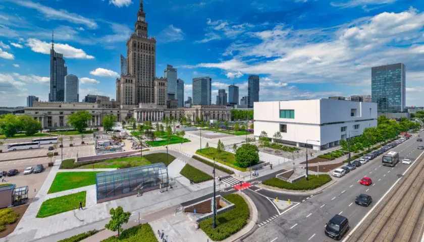 Warszawski plac defilad z Pałacem Kultury i Nauki, nowoczesnym budynkiem i ruchliwą ulicą.