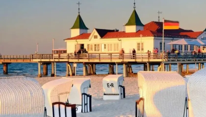 Zachód słońca nad morzem, molo z budynkiem i restauracją, plaża z koszami. Ahlbeck atrakcje zachęcają do spacerów.
