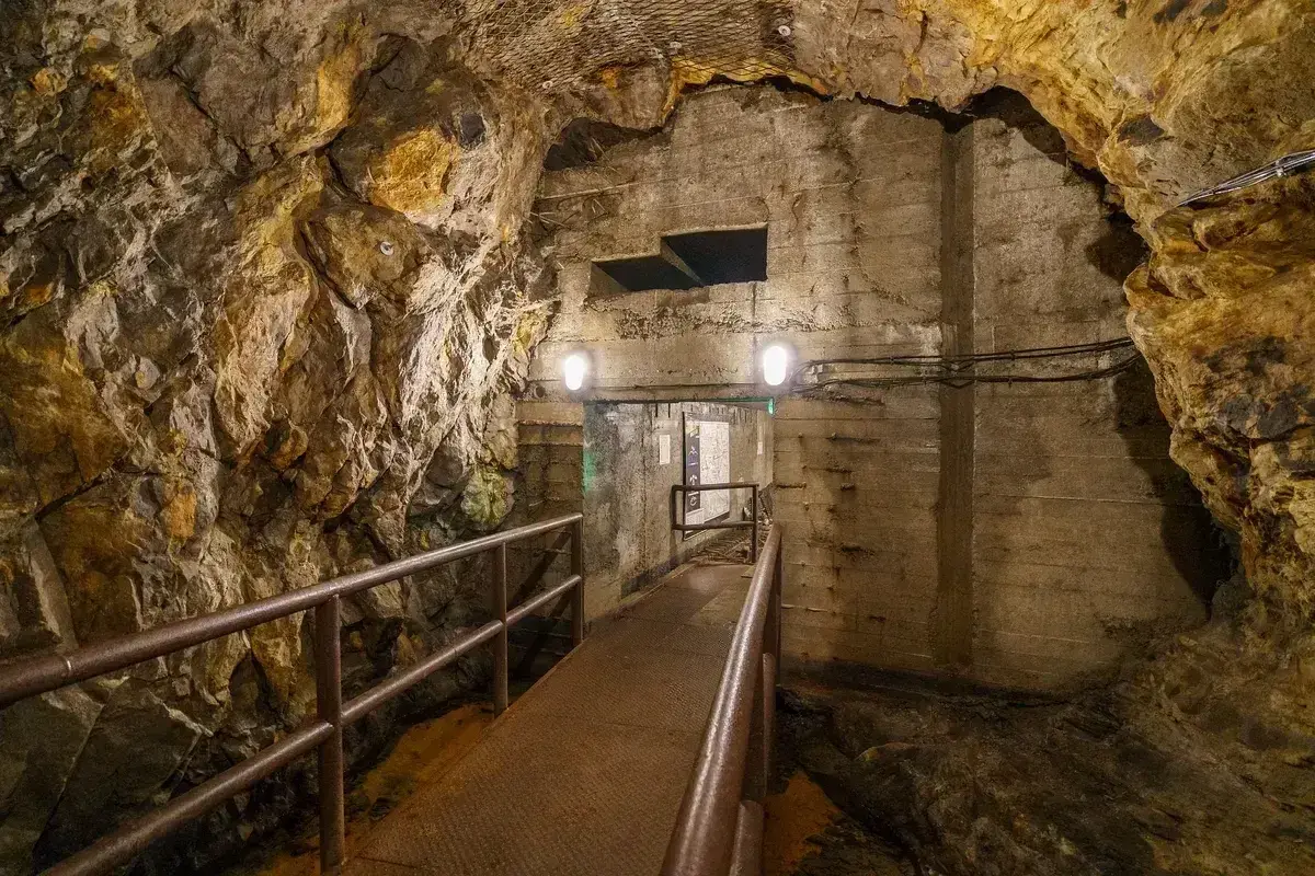Tunel w podziemiach Walimia, z metalową kładką i poręczą, prowadzi do oświetlonego przejścia. Odkryj te niezwykłe walim atrakcje.