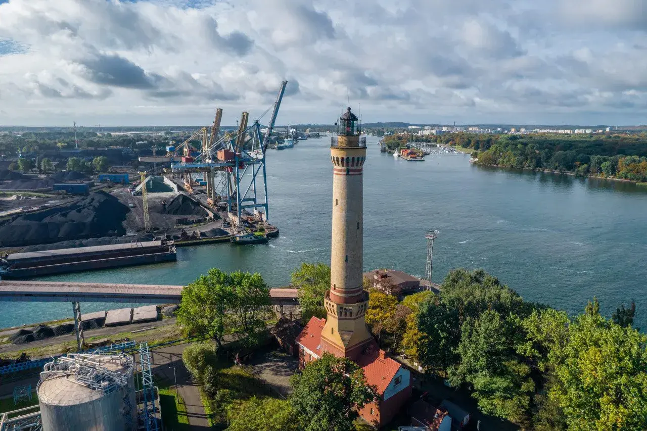 Latarnia morska góruje nad portem Świnoujście, gdzie widać dźwigi, statki i składy węgla.