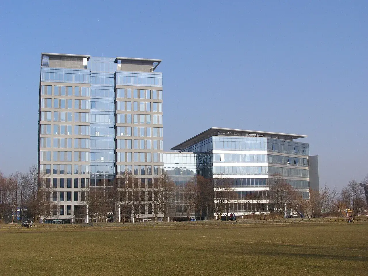 Nowoczesne budynki Olivia Tower i sąsiedni biurowiec z przeszklonymi fasadami, na tle błękitnego nieba.