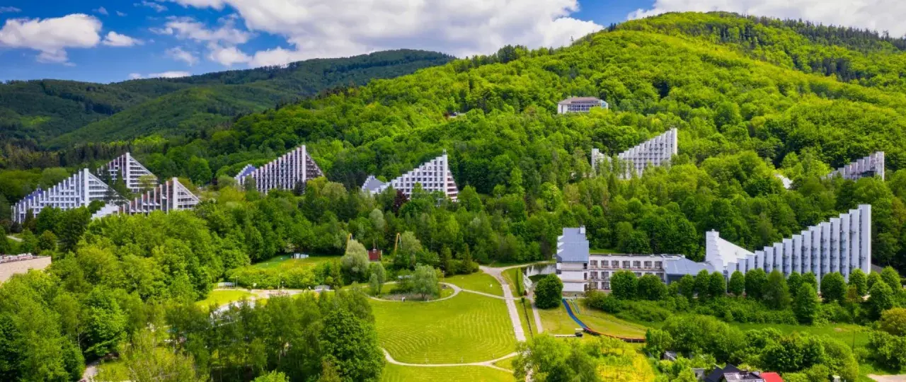 Nowoczesne budynki architektoniczne wkomponowane w zielone zbocza Beskidu Śląskiego. Uzdrowisko w Beskidzie Śląskim otoczone bujną roślinnością.