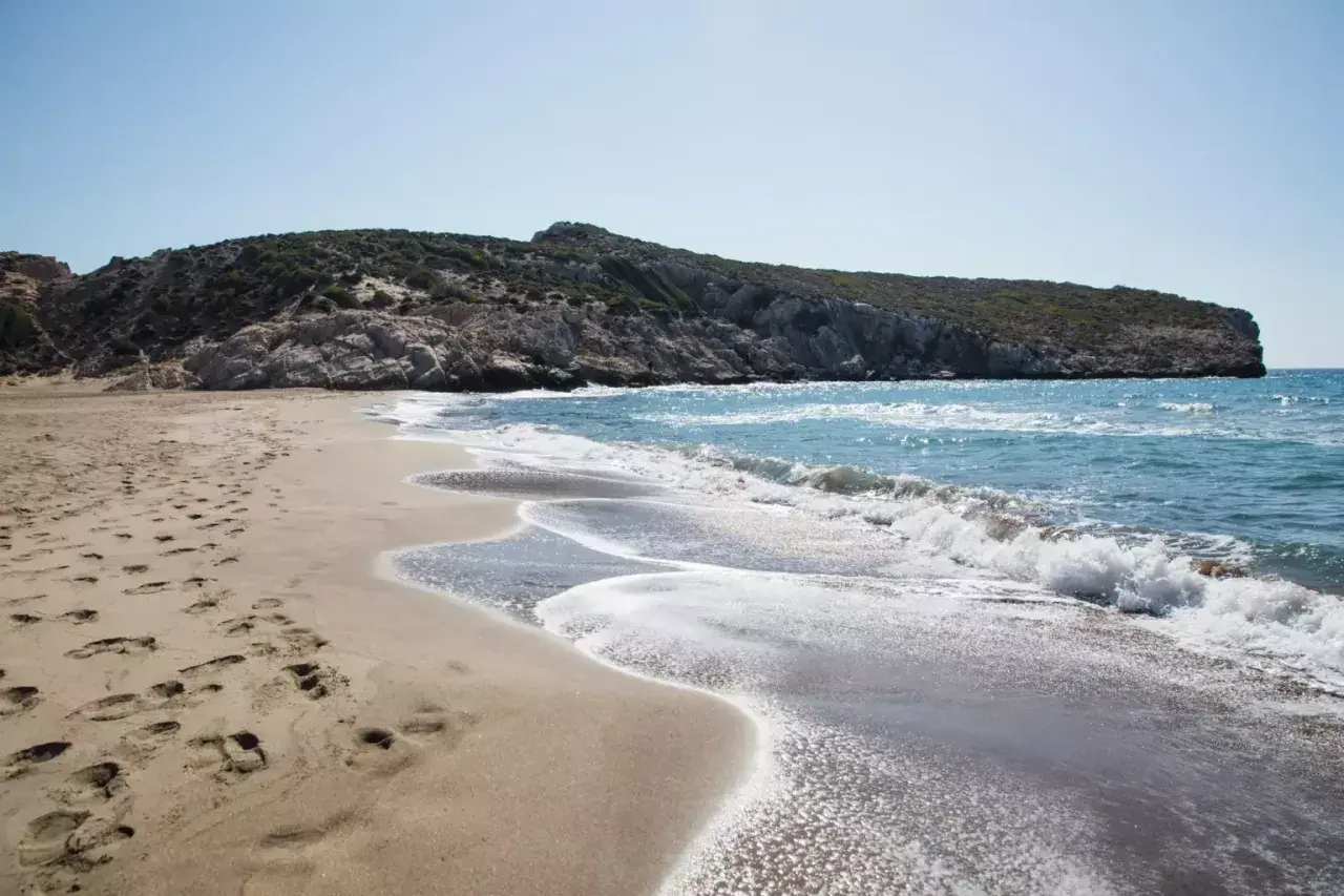 Piaszczysta plaża z falami i skalistym wzgórzem w tle.