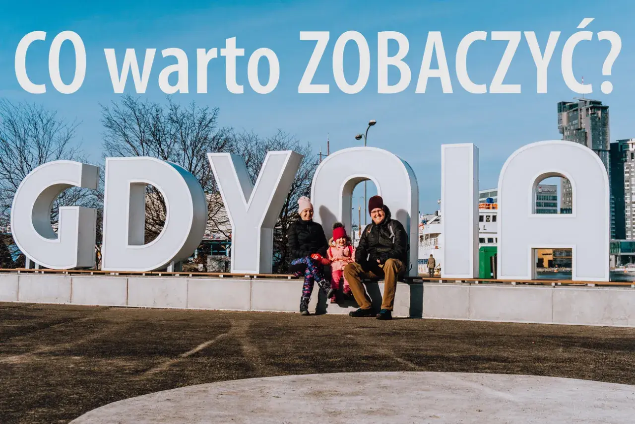 Rodzina pozuje przy napisie GDYNIA. W tle nowoczesne budynki, idealne na wakacyjne gdynia atrakcje dla dorosłych.