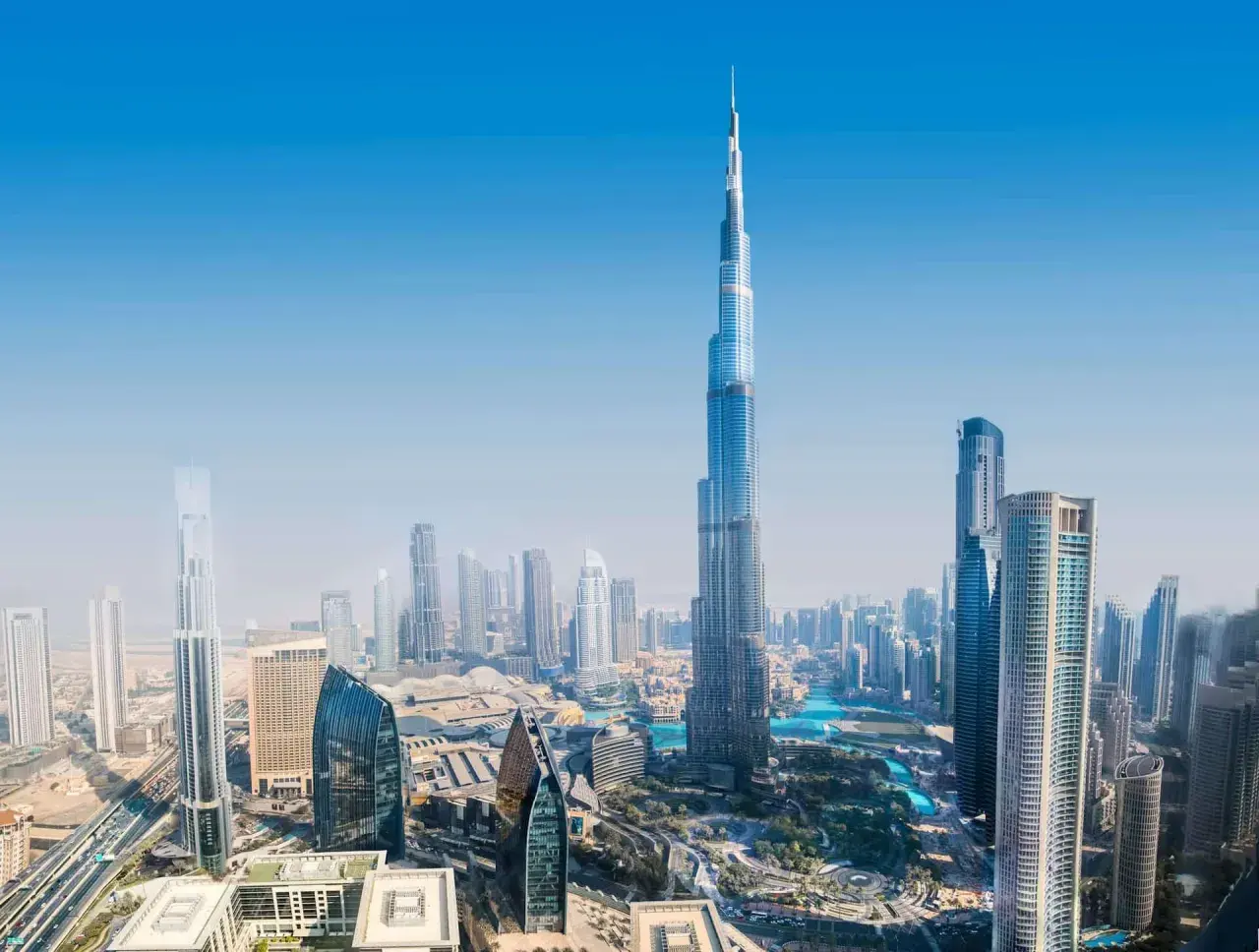 Widok z lotu ptaka na Dubaj, z dominującym Burdż Chalifa. Nowoczesne drapacze chmur i błękitne wody tworzą futurystyczny krajobraz.