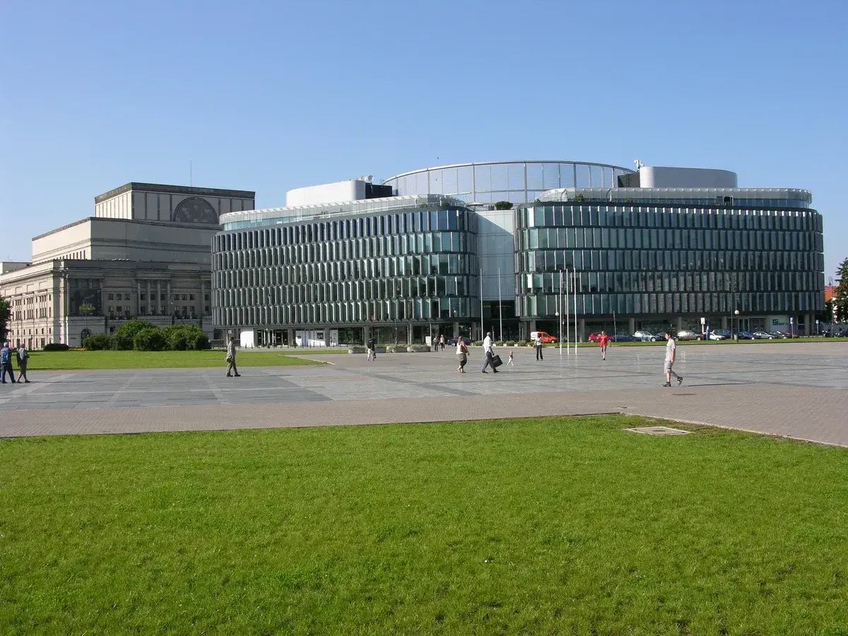 Plac Piłsudskiego w Warszawie. Nowoczesny budynek z przeszkloną fasadą obok klasycystycznego gmachu.