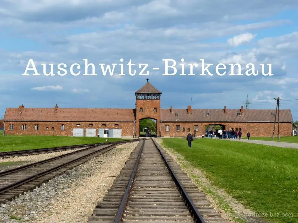Brama obozowa Auschwitz-Birkenau z wieżą i torami kolejowymi.