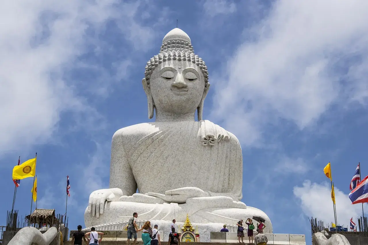 Wielki Budda na Phuket, majestatyczna biała statua na tle błękitnego nieba z chmurami. Turyści wchodzą po schodach.