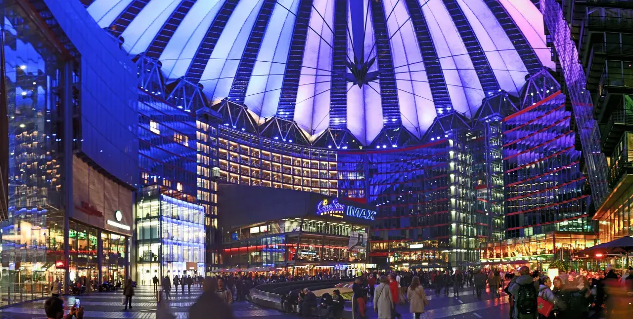Nocny widok na Sony Center w Berlinie, z oświetlonym dachem i fasadami budynków, pełen ludzi spacerujących po placu.