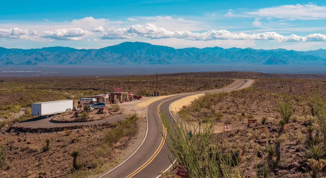 Droga Route 66 w pustynnym krajobrazie z budynkami i górami w tle.