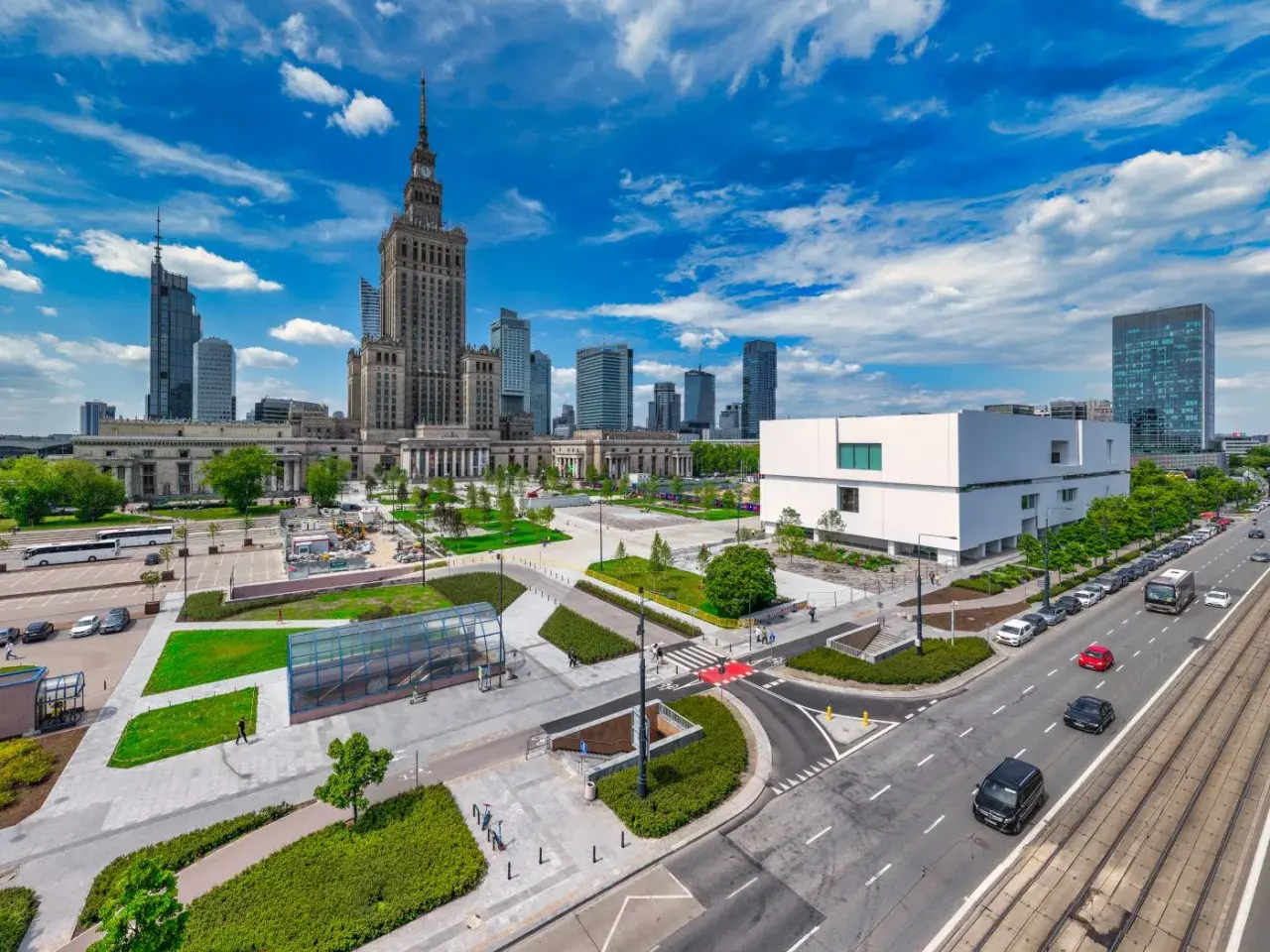 Warszawski plac defilad z Pałacem Kultury i Nauki, nowoczesnym budynkiem i ruchliwą ulicą.