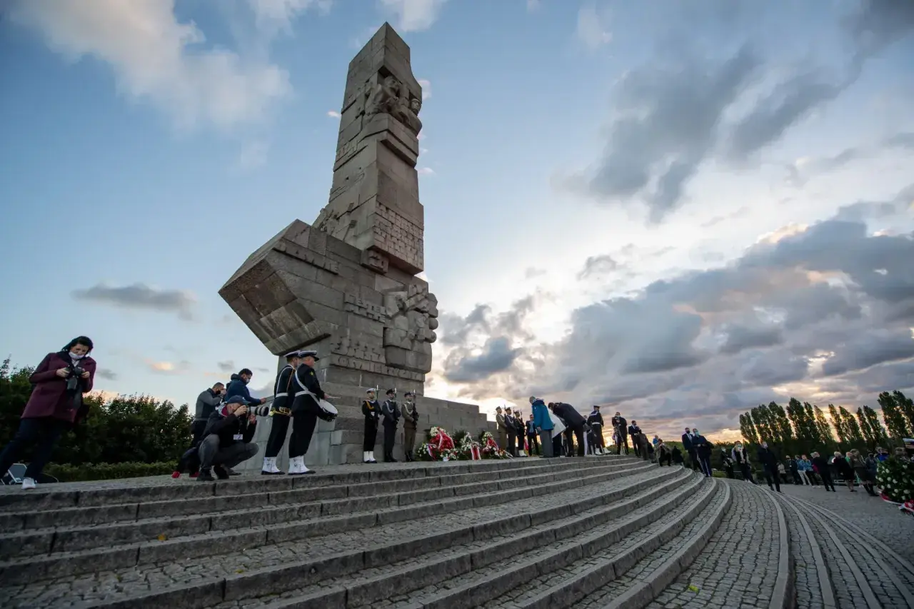 Uroczystość przy Pomniku Obrońców Wybrzeża na Westerplatte. W tle monumentalny monument, a na schodach delegacje i żołnierze.