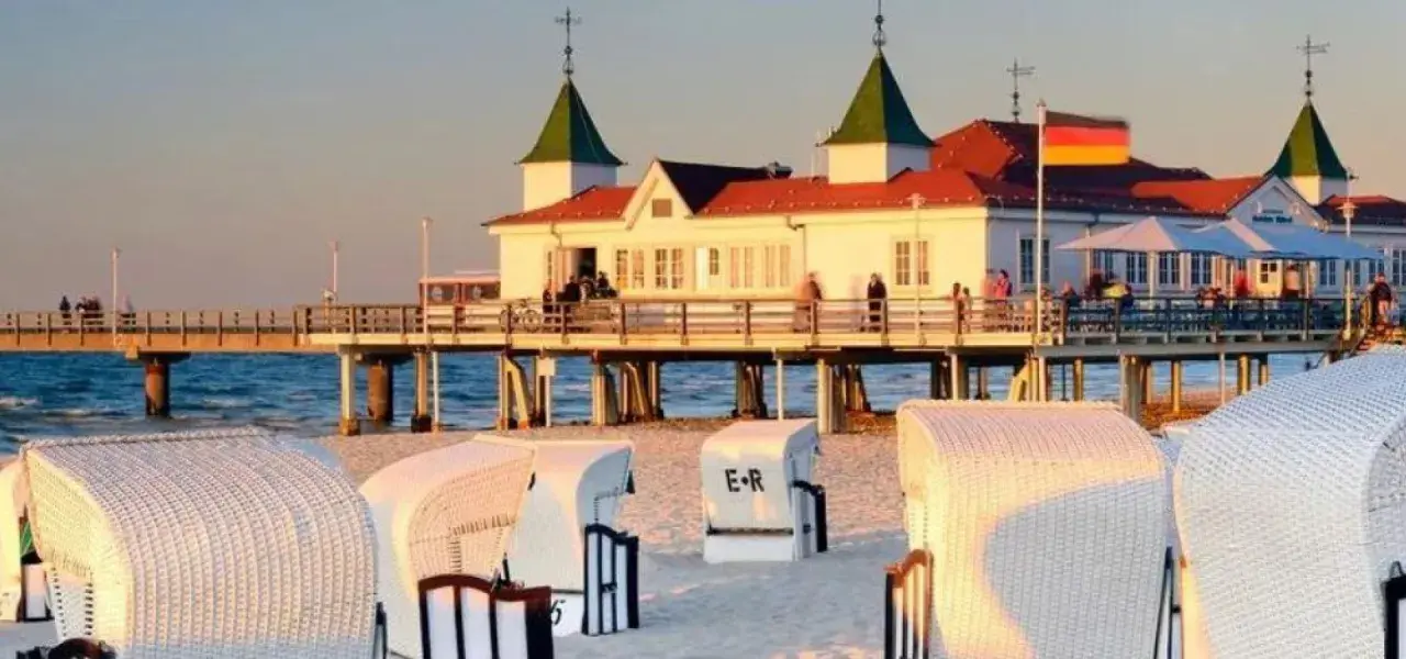 Zachód słońca nad morzem, molo z budynkiem i restauracją, plaża z koszami. Ahlbeck atrakcje zachęcają do spacerów.