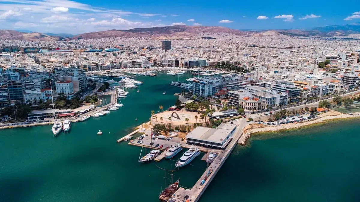 Widok z lotu ptaka na tętniący życiem piraeus port z licznymi jachtami i statkami, otoczony zabudowaniami i górami w tle.