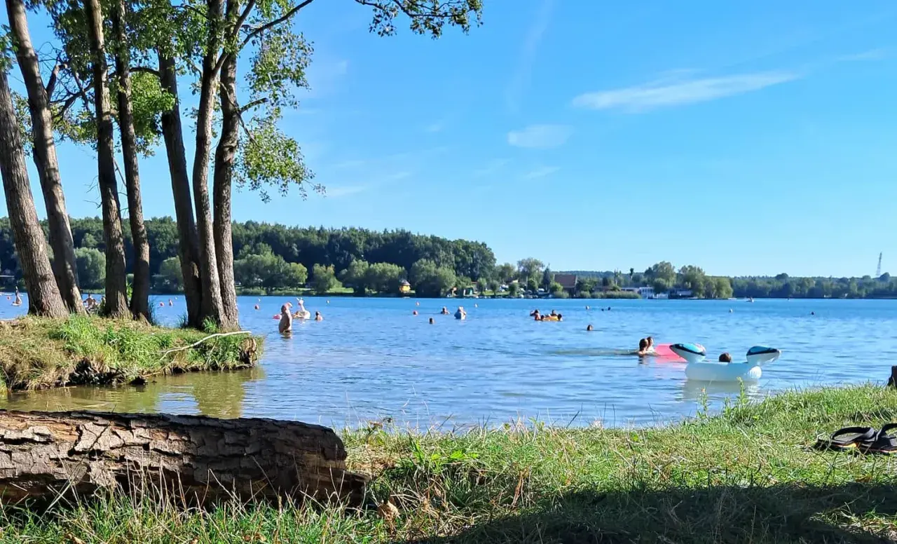 Słoneczny dzień nad jeziorem Pławniowice. Ludzie kąpią się i relaksują na dmuchanych zabawkach.