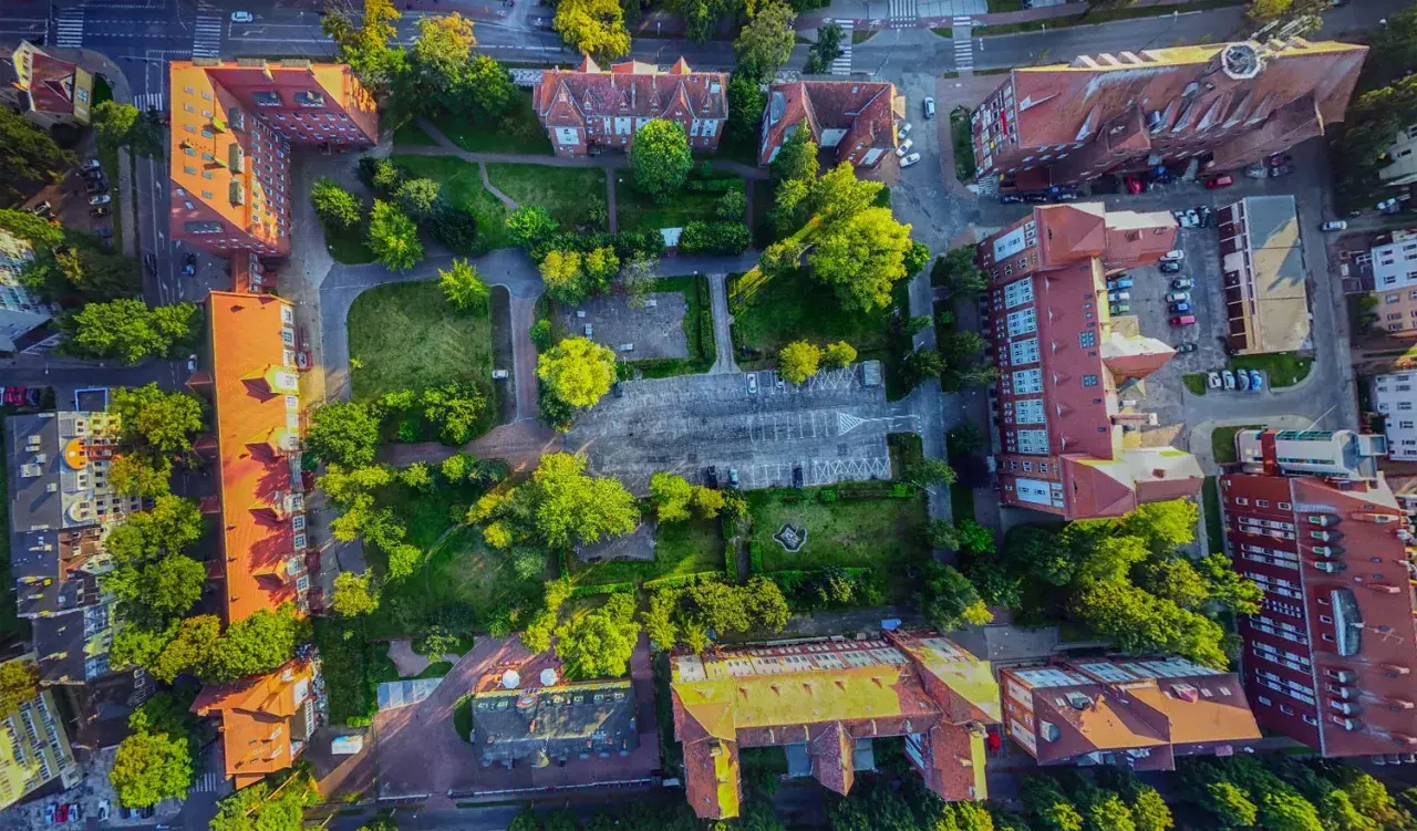 Widok z lotu ptaka na zabudowania i tereny zielone. Widać parking, budynki z czerwonymi dachami i drzewa. Promenada Świnoujście atrakcje w pełnej krasie.