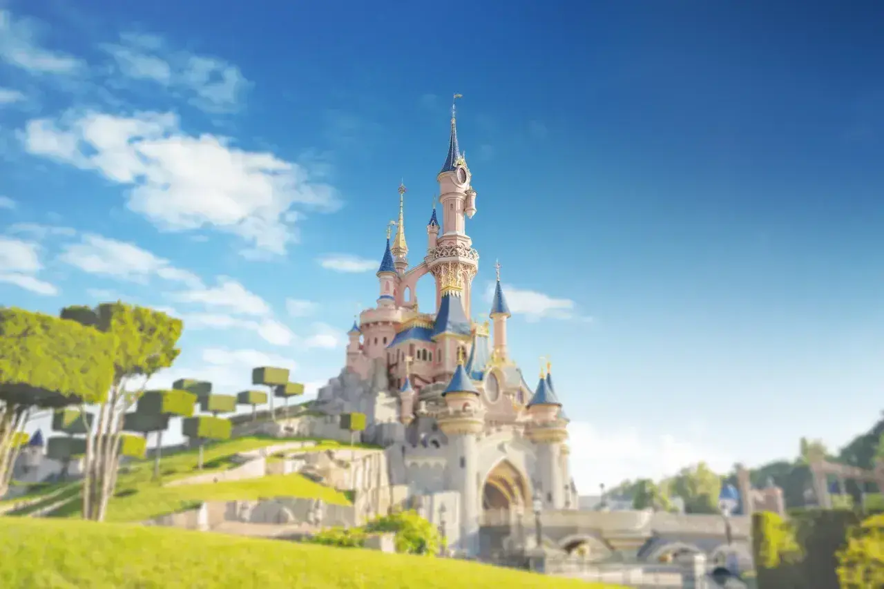 Zamek w Disneylandzie Paryż na tle błękitnego nieba z chmurami i zielonymi drzewami.