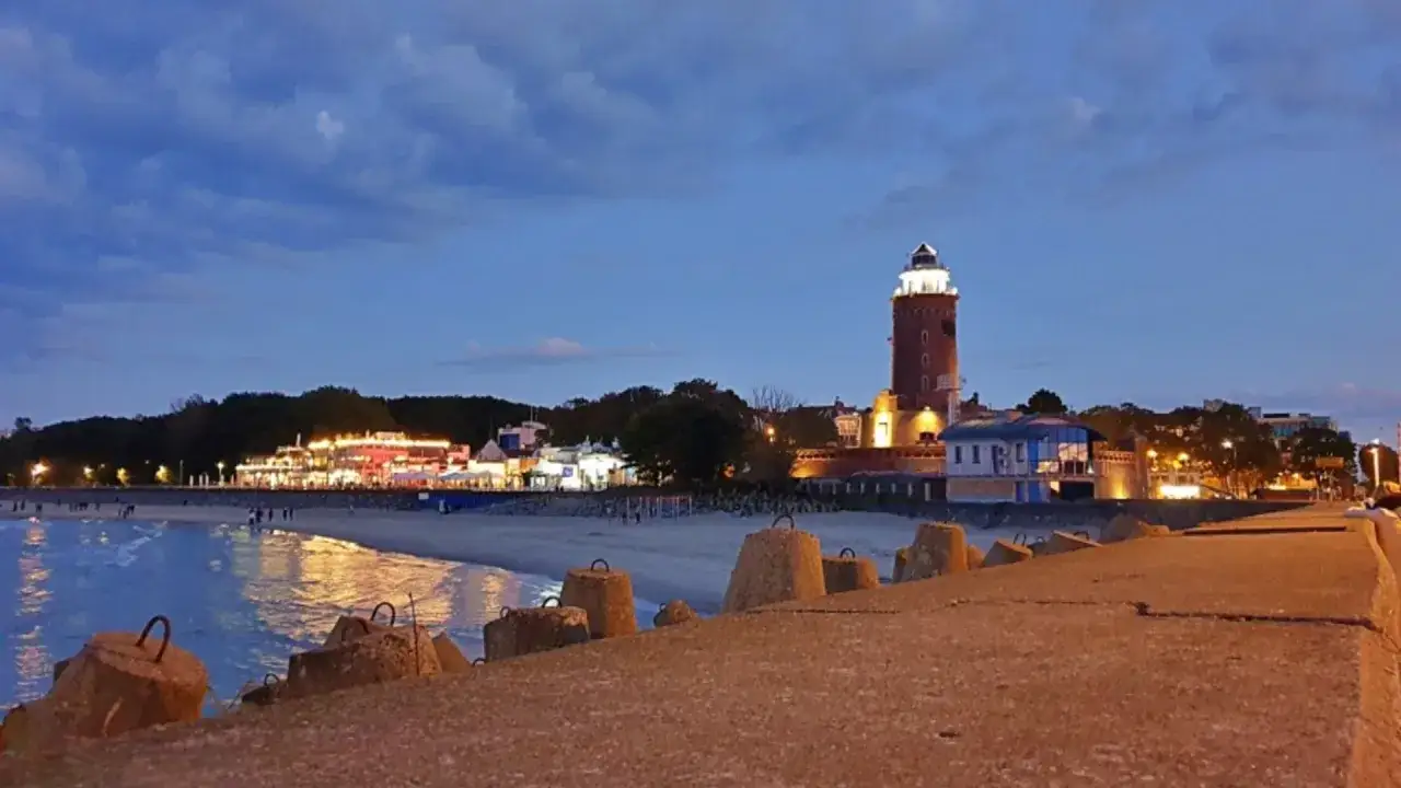 Wieczorny port w Kołobrzegu. Latarnia morska oświetla plażę i budynki nadmorskiej promenady.