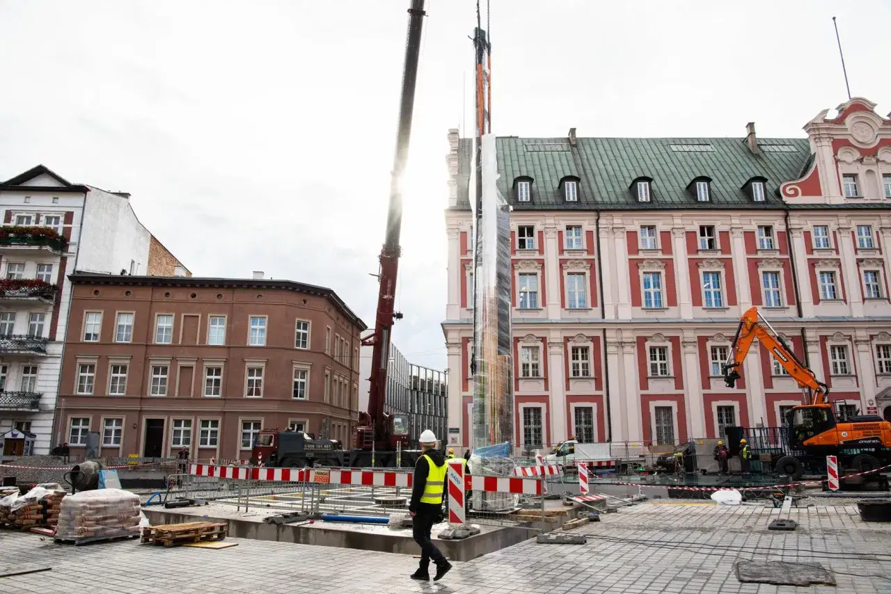 Plac Kolegiacki w Poznaniu. Trwa montaż nowoczesnej instalacji artystycznej. W tle zabytkowe kamienice i plac budowy.