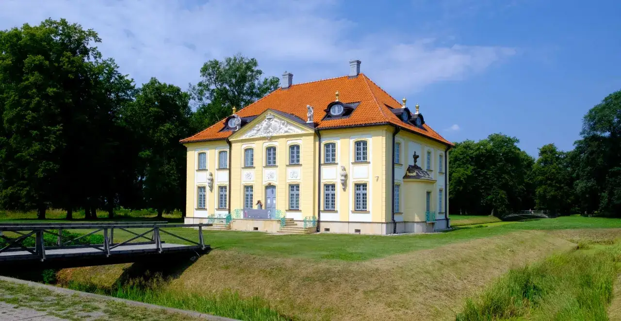 Pałac Branickich w Choroszczy, żółty, z pomarańczowym dachem, otoczony zielenią i fosą.