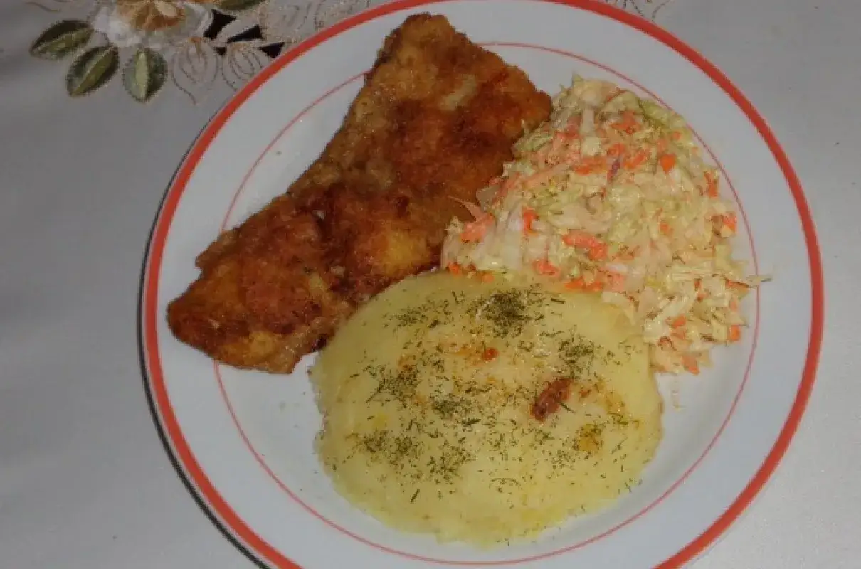 Złocista miruna w panierce, podana z puree ziemniaczanym posypanym koperkiem i chrupiącą surówką z marchewki i kapusty.