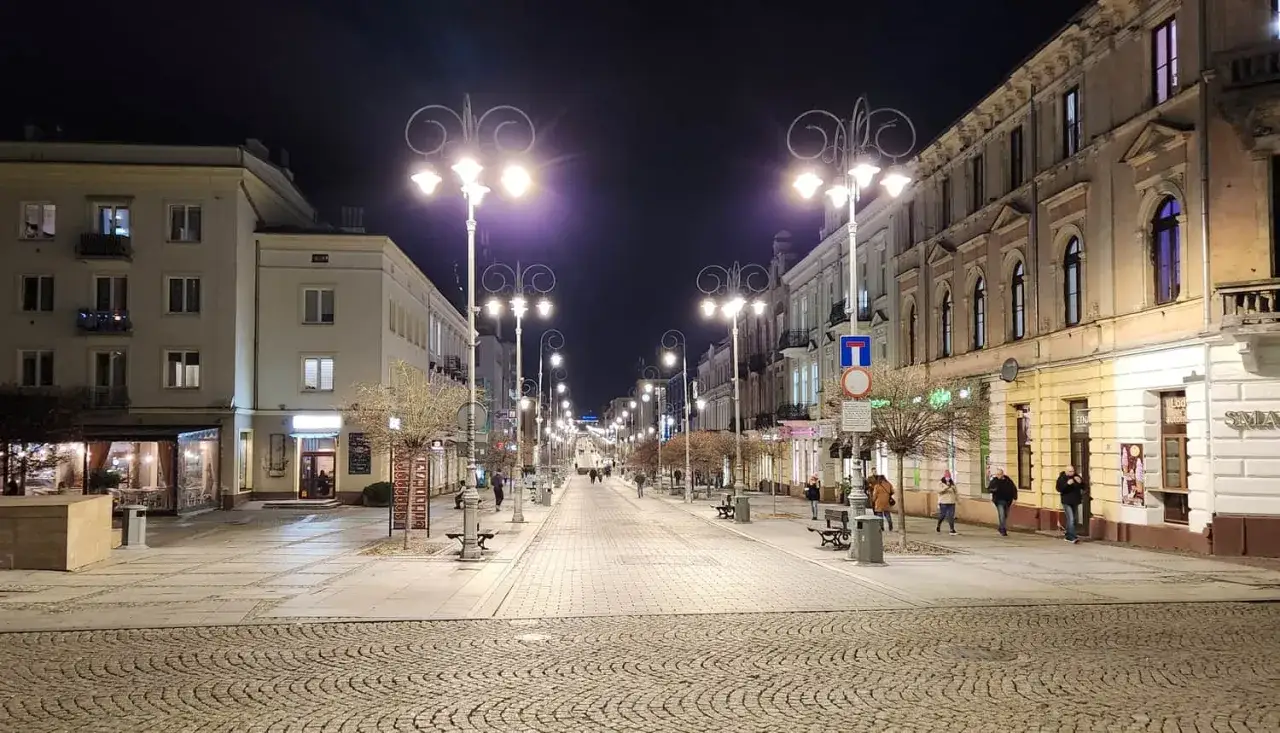 Nocny spacer po placu artystów w Kielcach. Oświetlona ulica z kamienicami i latarniami.