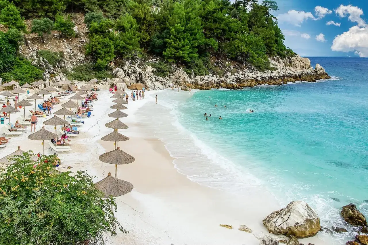 Rajska plaża z białym piaskiem, turkusową wodą i rzędami parasoli. Idealne miejsce na relaks, jak w hotelu Rachoni Imperial.