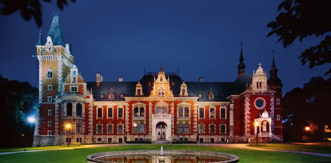 Pałac w Pławniowicach nocą, z fontanną na pierwszym planie. Wspaniałe atrakcje czekają na zwiedzających.