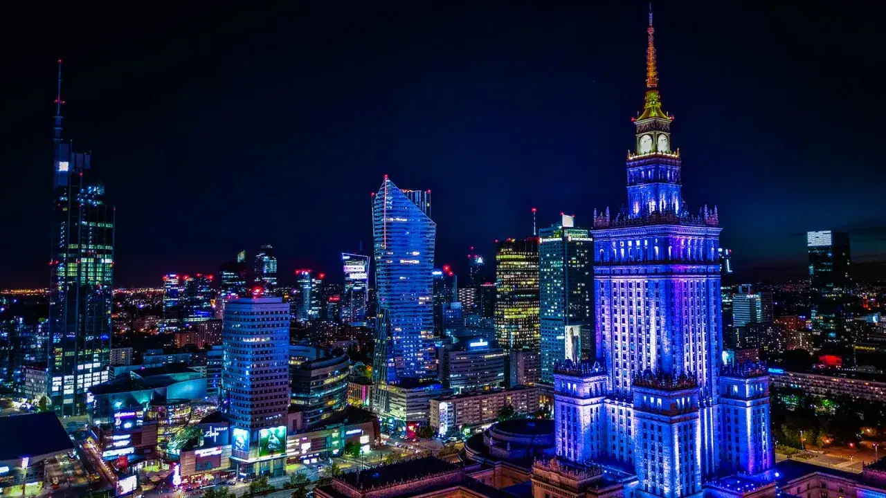 Warszawa nocą, rozświetlona wieżowcami. Widać Pałac Kultury i Nauki, nowoczesne budynki i światła miasta. Idealne miejsce na pobyt w jednym z courtyard hotels warsaw.