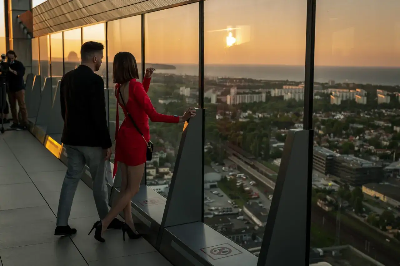 Para spaceruje po tarasie widokowym Olivia Tower, podziwiając zachód słońca nad miastem i morzem.