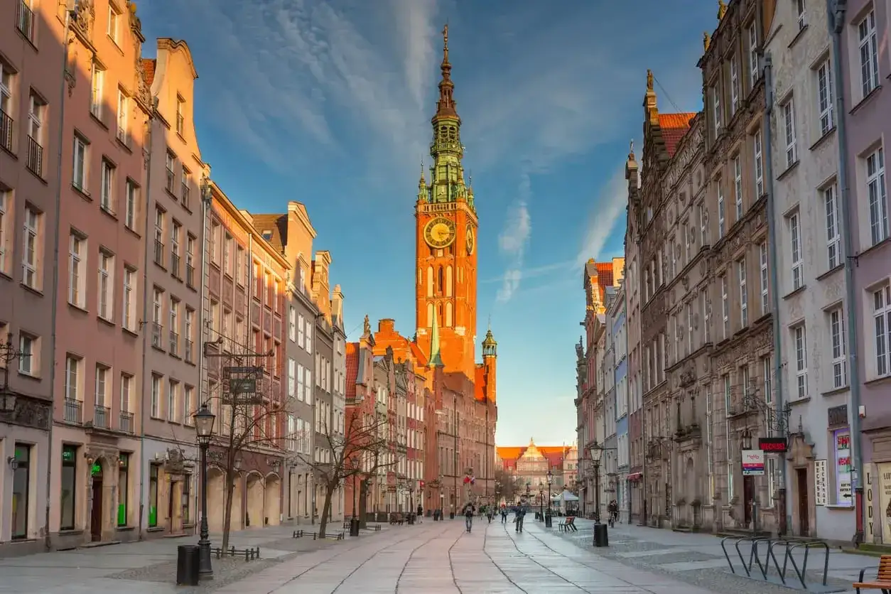 Długa ulica w Gdańsku z Ratuszem Głównym i kamienicami w słońcu.