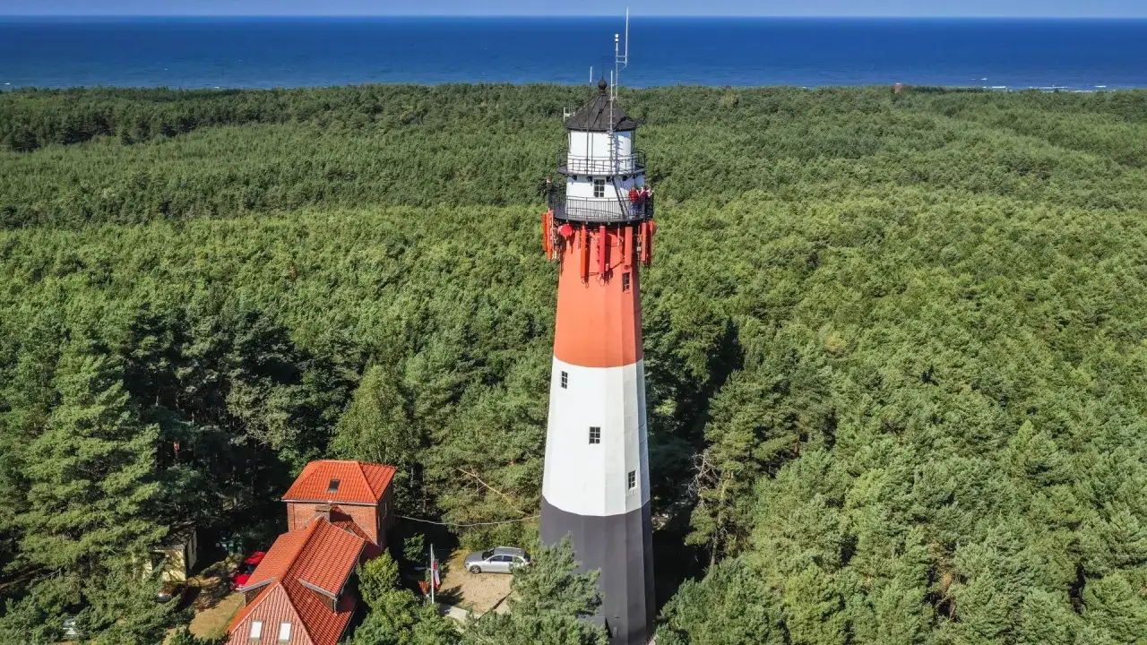 Latarnia morska góruje nad lasem, tworząc wrażenie głębia landsort. Morze w tle.