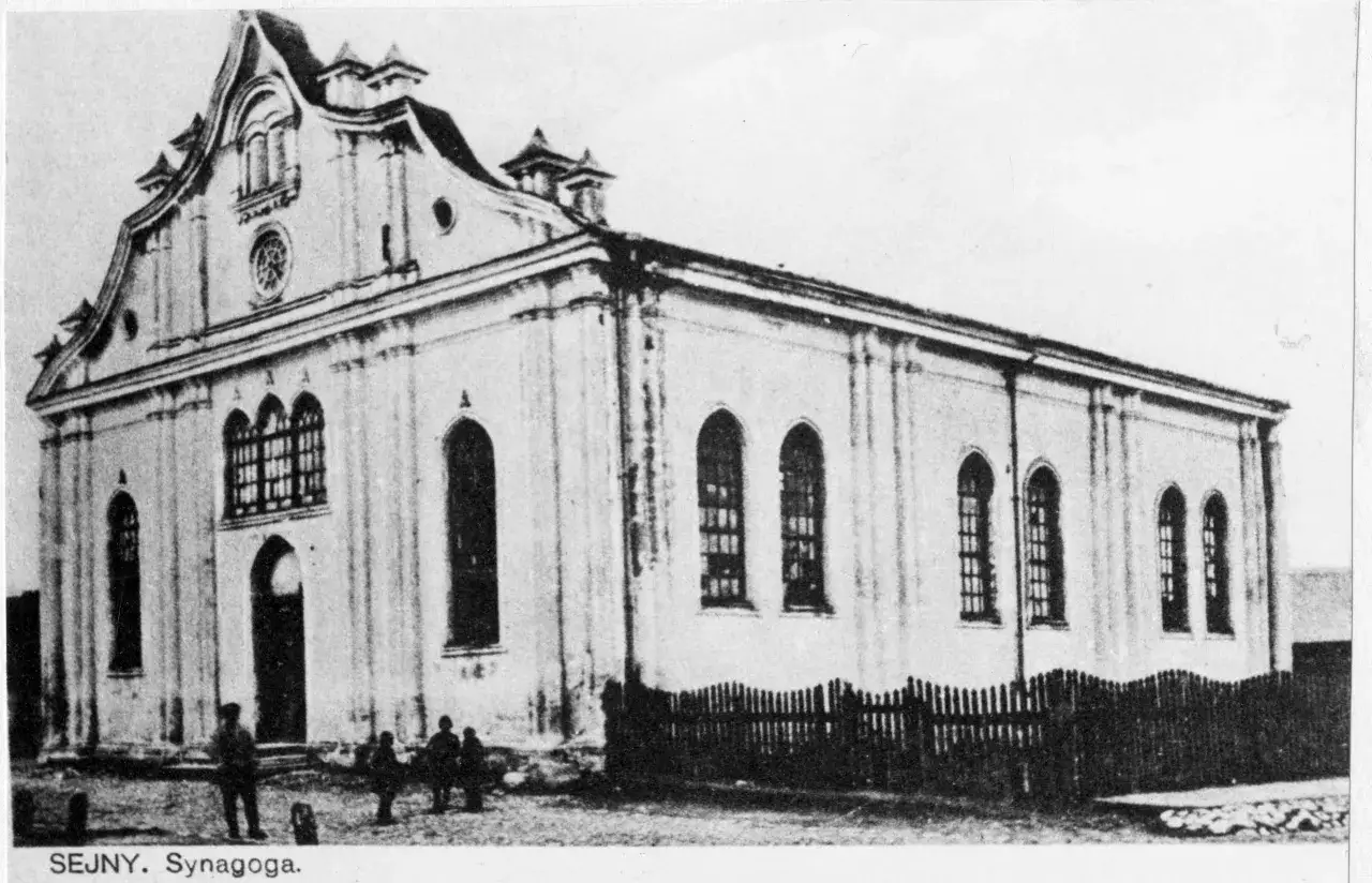 Synagoga w Sejnach, jedna z historycznych atrakcji miasta, z charakterystyczną fasadą i kilkoma postaciami przed wejściem.